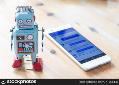 Toy robot and smartphone, symbol for chatbot and messenger