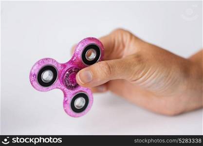 toys, entertainment and people - close up of hand playing with pink glittering fidget spinner. close up of hand playing with fidget spinner
