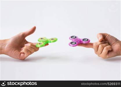 toys, entertainment and people - close up of two hands playing with fidget spinners and doing finger transfer trick. close up of two hands playing with fidget spinners
