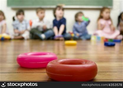 Toys on the floor and school children sitting in the background