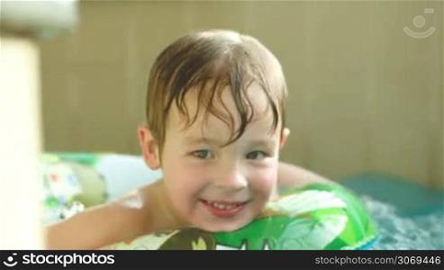 Tracking shot of a cute little boy enjoying swimming with rubber ring in the pool. Active and happy kid