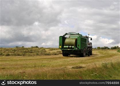 Tractor and Harvesting machine working in a green field.