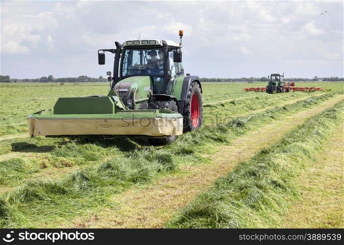 tractor and mower in green meadow in the netherlands on sunny day