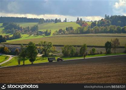Tractor on the field. Beautiful autumn nature with landscape in the Czech Republic. Colorful trees with blue sky and sun. Background for autumn and agriculture.