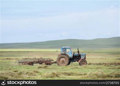 tractor raking dry hay in the field