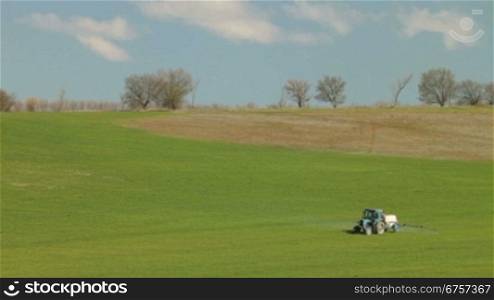 Tractor spraying a field of crops in spring