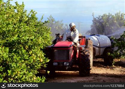 Tractor spraying pesticide and insecticide on lemon plantation in Spain. Weed insecticide fumigation. Organic ecological agriculture. A sprayer machine, trailed by tractor spray herbicide. Tractor spraying pesticide and insecticide on lemon plantation in Spain. Weed insecticide fumigation. Organic ecological agriculture. A sprayer machine, trailed by tractor spray herbicide.