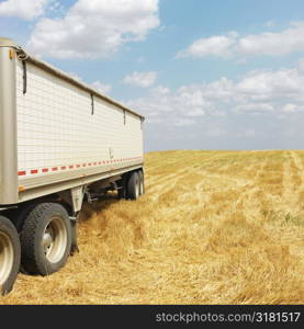 Tractor trailer truck in harvested crop field.