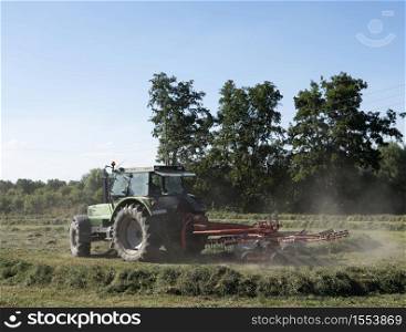 tractor with grass shaker in dry french summer country landscape with trees