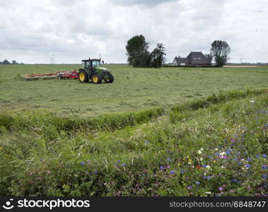 tractor with grass turner near farm in dutch province of Friesland near Leeuwarden and summer flowers