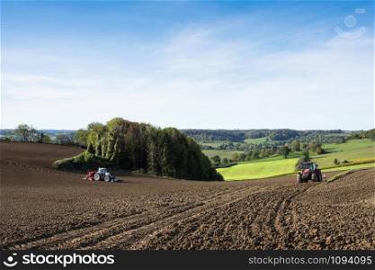 tractor with harrow on field in beautiful countryside of south limburg in the netherlands on sunny day in the fall under blue sky