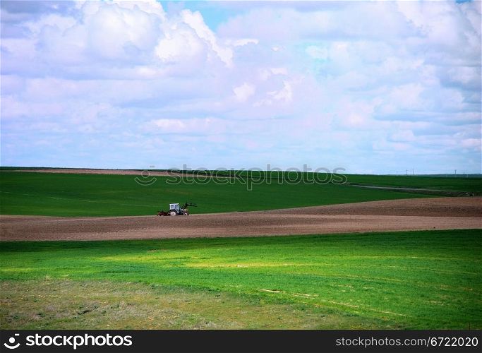 Tractor working in the green field under a cloudy blue sky . Tractor working in the field
