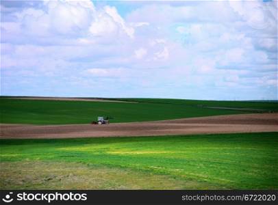 Tractor working in the green field under a cloudy blue sky . Tractor working in the field