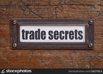 trade secrets text - file cabinet label, bronze holder against grunge and scratched wood