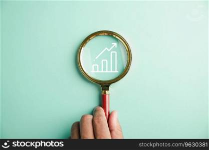 Trader attention to detail, Holding magnifier glass, hand inspects bar graph with rising arrow. Analyzing technical stock market chart defines business investment and the pursuit of financial success.