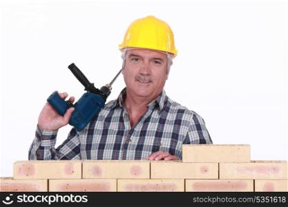 Tradesman holding a power tool and standing behind a brick wall