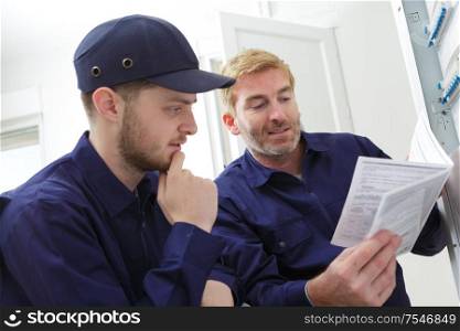 tradesman looking at instruction book by circuit breaker box