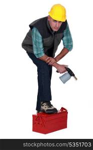 Tradesman posing with his foot propped on a toolbox and holding a spray gun