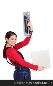 Tradeswoman holding up a tile cutting machine and a tile