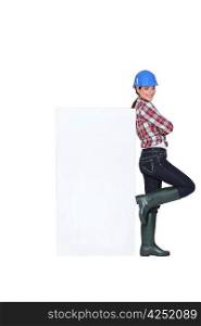 Tradeswoman leaning against a blank sign