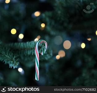Traditional artificial Christmas tree with candy cane and white lights glowing in background