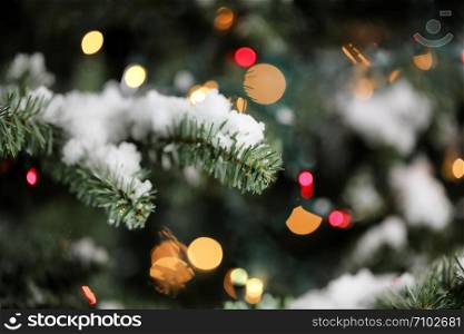 Traditional artificial Christmas tree with glowing lights and snow in background