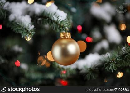 Traditional artificial Christmas tree with golden ball ornament with glowing colorful lights and snow in background