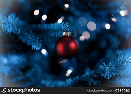 Traditional artificial Christmas tree with red ball ornament and white lights glowing in vintage format