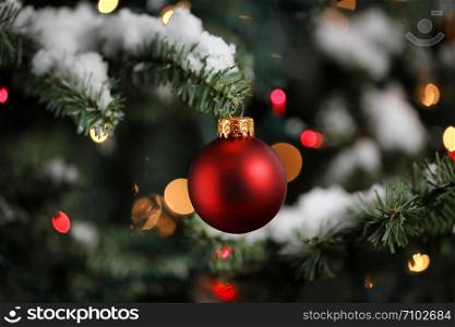 Traditional artificial Christmas tree with red ball ornament with glowing colorful lights and snow in background