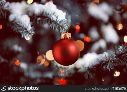 Traditional artificial Christmas tree with red ball ornament with glowing colorful lights and snow in vintage format layout
