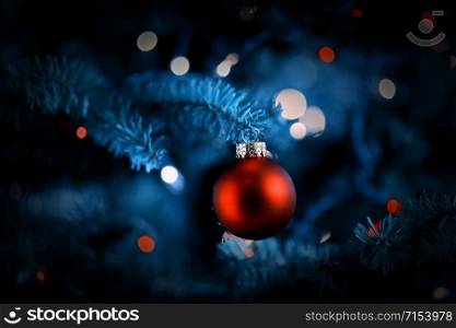 Traditional artificial Christmas tree with single red ball ornament and glowing colorful lights in vintage format