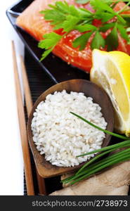 traditional asian ingredients (Fresh salmon steak filet, uncooked rice, ginger, lemon, and chopsticks) over white