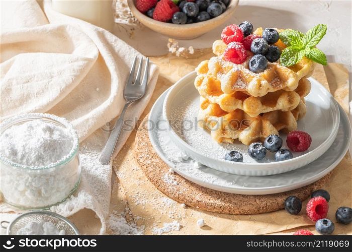 Traditional Belgian waffles with fresh raspberries and blueberries sprinkled with powdered sugar on the kitchen counter.