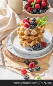 Traditional Belgian waffles with fresh raspberries and blueberries sprinkled with powdered sugar on the kitchen counter.