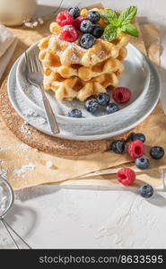 Traditional Belgian waffles with fresh raspberries and blueberries sprinkled with powdered sugar on the kitchen counter.