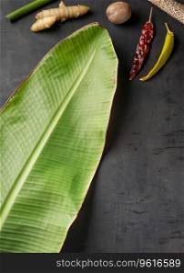 Traditional blank banana leaf with spices on dark background with space for text