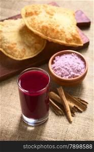 Traditional Bolivian Api, a purple corn beverage, with pastel (deep-fried pastry filled with cheese) in the back, photographed with natural light (Selective Focus, Focus in the middle of the drink&rsquo;s surface)