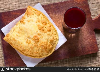 Traditional Bolivian snack called Pastel (deep-fried pastry filled with cheese) served with Api, a purple corn beverage on wooden board, photographed with natural light (Selective Focus, Focus on the pastry)