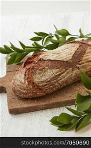 Traditional bread on a wooden board with branches of green leaves. Homemade fresh bread with leaves