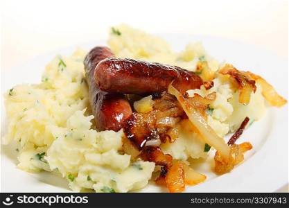 Traditional British &acute;bangers and mash&acute; meal of sausages with mashed parsley potatoes and caramelised onions on a plate.