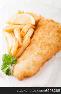 Traditional British Fish and Chips on chopping board and lemon slice on white stone background.
