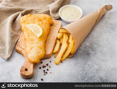Traditional British Fish and Chips with tartar sauce on chopping board on white table background.