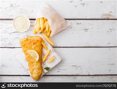 Traditional British Fish and Chips with tartar sauce on chopping board on white wood background.