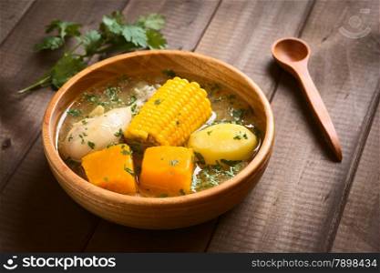 Traditional Chilean Cazuela de Pollo (or Cazuela de Ave) soup made of chicken, sweetcorn, pumpkin and potato, seasoned with fresh coriander served in wooden bowl, photographed on wood with natural light (Selective Focus, Focus one third into the soup)