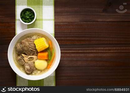 Traditional Chilean Cazuela de Vacuno or Cazuela de Carne, a beef soup with potato, corn, pumpkin, carrot, bell pepper, onion and rice, cut parsley on the side, photographed overhead on dark wood with natural light. Chilean Cazuela de Vacuno or Carne, Beef Soup