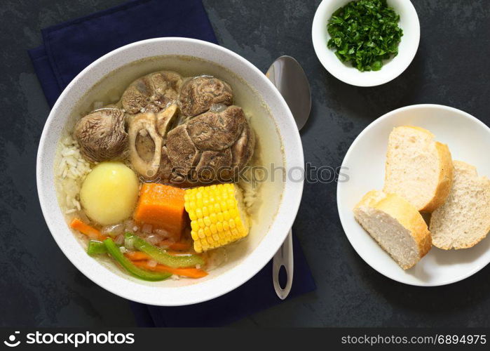 Traditional Chilean Cazuela de Vacuno or Cazuela de Carne, a beef soup with potato, corn, pumpkin, carrot, bell pepper, onion and rice, cut parsley and bread slices on the side, photographed overhead on slate with natural light. Chilean Cazuela de Vacuno or Carne, Beef Soup