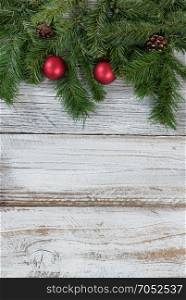 Traditional Christmas evergreen branches with red ball ornaments decorations on rustic knotty wood in flat lay format