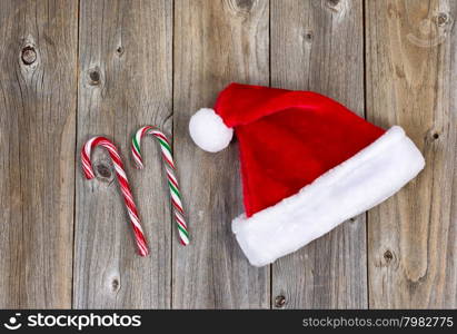 Traditional Christmas Santa cap and candy canes on rustic wood. Boards in vertical pattern.