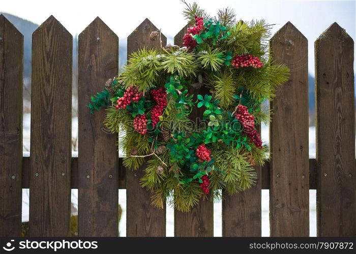 Traditional Christmas wreath with red berries hanging on wooden fence