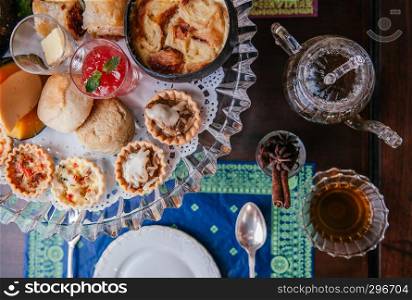 Traditional elegance English afternoon tea with scone, assorted tart and puff pastries on old wood table with tea pot and tea cup top view